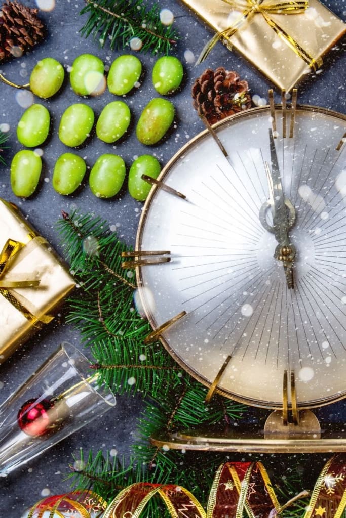 Twaalf druiven, een klok die middernacht slaat en feestelijke decoratie, symbool voor de Spaanse nieuwjaarstraditie Las doce uvas de la suerte tijdens de feestdagen aan de Costa del Sol, gepresenteerd door MDR Luxury Homes